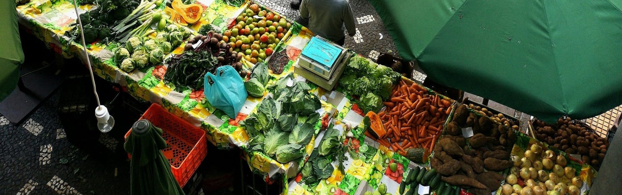 people standing near patio umbrella surrounded with fruits and vegetable stalls